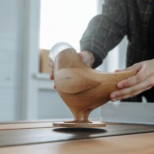 Close-up of hands carefully holding a handmade wooden bird sculpture, showcasing artisan craftsmanship and design.